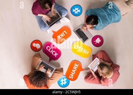 Überblick über vier junge zeitgenössische Freunde liegen und sitzen auf dem Boden und mit mobilen Gadgets während Social Networking Stockfoto