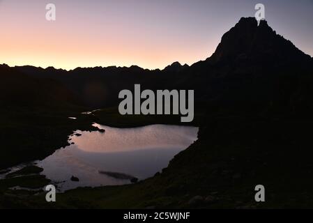 Morgendämmerung in den französischen Bergen der Pyrenäen. Der Himmel ist bunt. Die Silhouette eines großen Berges erscheint über einem schönen kleinen See. Stockfoto