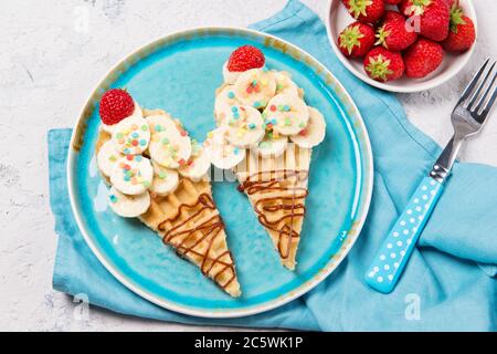 Süße Waffeln mit Banane und Erdbeere in Form von Eiskegel, Mahlzeit für Kinder Idee, Draufsicht Stockfoto