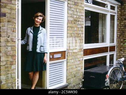 Attraktive Frau, die in den 1960er Jahren in einem modernen Haus in Hampstead, London, England, Großbritannien, vor der Haustür stand Stockfoto