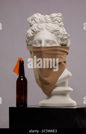 Statue einer Büste von Apollos Kopf in einem Kopftuch, das sein Gesicht bedeckt und mit einer Flasche Molotow-Cocktail Stockfoto