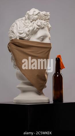 Statue einer Büste von Apollos Kopf in einem Kopftuch, das sein Gesicht bedeckt und mit einer Flasche Molotow-Cocktail Stockfoto