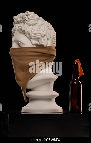 Statue einer Büste von Apollos Kopf in einem Kopftuch, das sein Gesicht bedeckt und mit einer Flasche Molotow-Cocktail Stockfoto