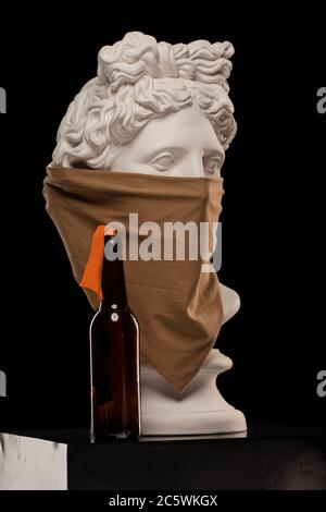 Statue einer Büste von Apollos Kopf in einem Kopftuch, das sein Gesicht bedeckt und mit einer Flasche Molotow-Cocktail Stockfoto