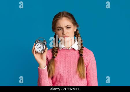 Überschlaf-Konzept. Müde Teenager Mädchen mit Zöpfen hält Wecker in ihren Händen Stockfoto