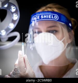 Eine Krankenschwester, die eine persönliche Schutzausrüstung trägt, einschließlich Gesichtsmaske und Gesichtsschutz, bereitet eine Spritze in einer Krankenhausumgebung vor. Stockfoto