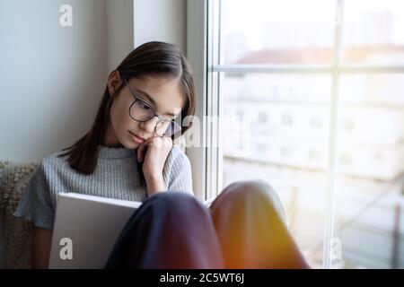 Nettes Teenager Mädchen Buch zu Hause lesen, während auf Fensterbank sitzen Stockfoto