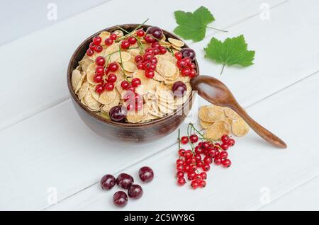 Frische Cornflakes mit Johannisbeeren und Kirschen in einer runden Schüssel auf Holzgrund. Stockfoto