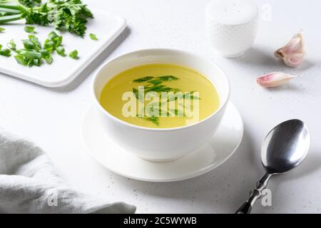 Hühnerbrühe mit grünen Zwiebeln in weißer Schüssel auf weißem Tisch. Speicherplatz kopieren. Stockfoto