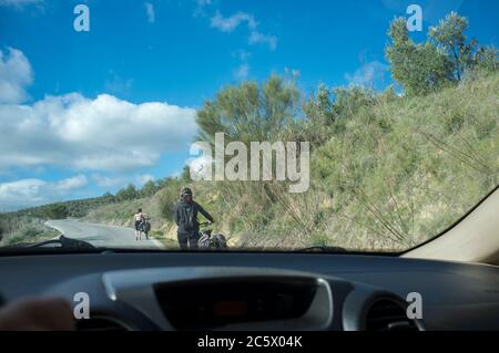 Langsam hinter zwei Wanderradlern auf Landstraße fahren. Manchmal schieben Radfahrer Fahrrad den Berg hinauf Stockfoto