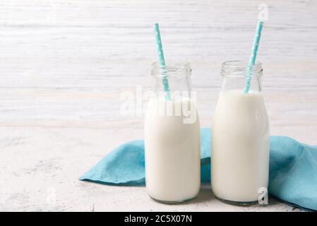 Zwei Flaschen Milch mit blauen Strohhalmen auf Holzgrund mit blauem Handtuch Stockfoto