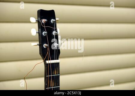Gitarrenhals und -Kopf in schlechtem Zustand mit gebrochenen Saiten vor der Hauswand Seitenansicht aus nächster Nähe Stockfoto