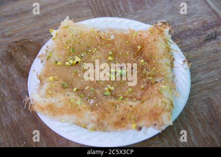 Eine Scheibe des Kanafeh, einer traditionellen nahöstlichen leckeres Dessert, in einem weißen Teller serviert Stockfoto