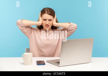 Ich möchte nicht mehr zuhören. Irritierte Angestellte, die mit einem Laptop am Arbeitsplatz sitzt, Ohren bedeckt und sich unzufrieden runzelt, sich über laute Geräusche ärgert Stockfoto