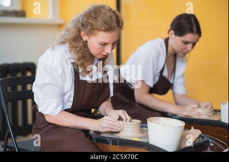 Zwei Frauen machen Keramik auf einem Töpferrad, Formen Ton durch ihre Hände, Nahaufnahme. Töpferwerkstatt im Kunststudio. Stockfoto
