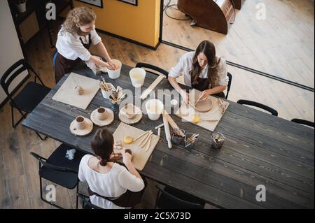 In der Tonwerkstatt. Töpferinnen sprechen und lächeln während des Arbeitsprozesses in der Tonwerkstatt. Weibliche Töpfer Meister Rollen den Ton auf Stockfoto