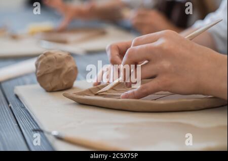 Nahaufnahme des weiblichen Töpfers, der Stock hält und Ornament auf Steingut macht. Clay Master Formung Clay Produkt. Konzept der keramischen Kunst und Hobby. Stockfoto