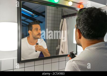 Ein hübscher Mann rasiert sich mit der Trimmermaschine vor dem Badezimmerspiegel Stockfoto
