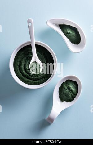 Grüne Chlorella oder Spirulina Pulver in drei unterschiedlich geformten weißen Porzellanschalen und in kleinen Löffel auf blauem Hintergrund. Gesunde Superfood-Essen Stockfoto