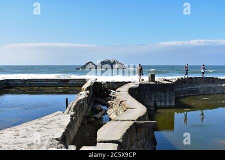 Drei Besucher, die entlang der Ruinen der Sutro Bäder in Lands End, San Francisco. Der Pazifik und Seal Rocks als Hintergrund und blauer Himmel. Stockfoto