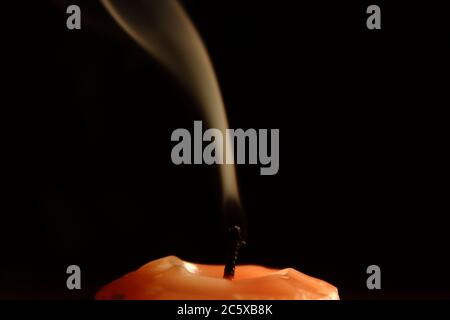 Erloschene orange Kerze auf dunklem Hintergrund mit Rauchdeteai Stockfoto
