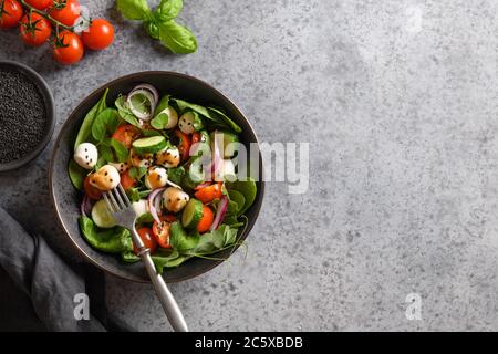 Salat mit Spinat, Kirschtomaten, Zwiebel und Mozzarella auf grauem Steingrund. Draufsicht. Stockfoto