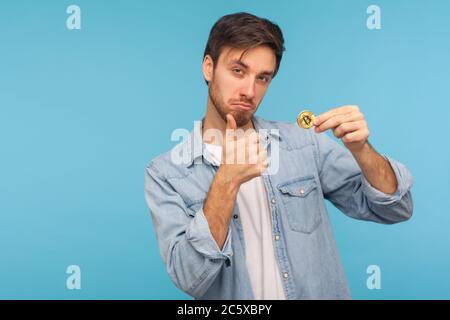 Ich mag Kryptowährung! Positive Geschäftsmann in Denim-Shirt hält Bitcoin und zeigt Daumen nach oben Geste, zufrieden mit goldenen BTC-Münze, elektronische m Stockfoto