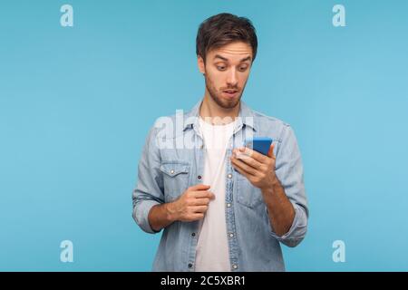 Porträt des staunenden Mannes in Arbeiter Denim Shirt lesen schockierende Nachricht auf Handy, überrascht von unerwarteten Nachrichten, mit mobilen App für Online-Chat Stockfoto