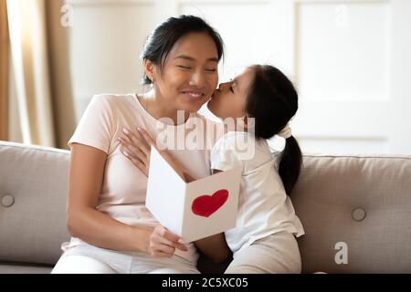 Nette kleine vietnamesische Baby Mädchen küssen lächelnde Mama, gratuliert drinnen. Stockfoto