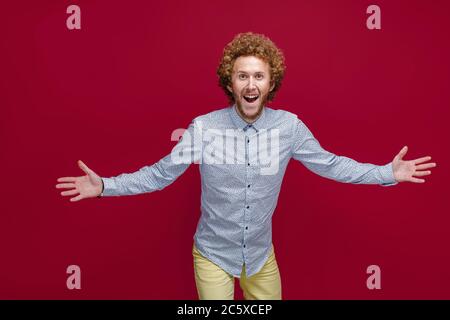 Junger lockiger reifer Mann, der ein elegantes Hemd trägt und einen Sieg oder Erfolg feiert, ist überrascht und schockiert. Stockfoto