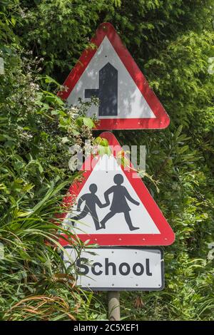 Ländliche Land Schule dreieckiges Warnschild in Straßenhecke. UK Junge und Mädchen zu Fuß Piktogramm für Sicherheitsbewusstsein. Metapher zurück in die Schule. Stockfoto