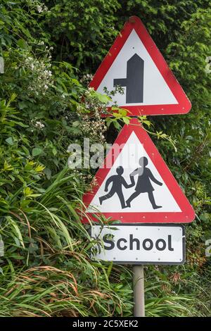 Ländliche Land Schule dreieckiges Warnschild in Straßenhecke. UK Junge und Mädchen zu Fuß Piktogramm für Sicherheitsbewusstsein. Metapher zurück in die Schule. Stockfoto