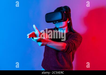 Frau mit Virtual-Reality-Brille auf dem Kopf spielen Shooter-Spiel, Zeigefinger Pistole und schießen direkt auf das Ziel, Töten im Cyberspace mit VR-Kopf Stockfoto
