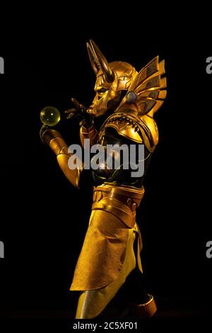 Ein männlicher Schauspieler in einem Anzug einer ägyptischen Mythologie-Figur, die goldene Gottheit Jackal Anubis, verdreht Buugeng in gelbem Licht auf schwarzem Hintergrund Stockfoto