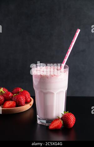 Frischer Milchshake mit Erdbeeren auf schwarzem Hintergrund. Sommergetränk mit einem Stroh in einem Glas. Für Text platzieren. Stockfoto