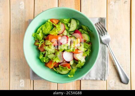 Rezept für Gemüsesalat mit Tomaten, Gurken und Radieschen. Saisonales Gericht auf Holzgrund. Veganes Essen für die Ernährung. Stockfoto