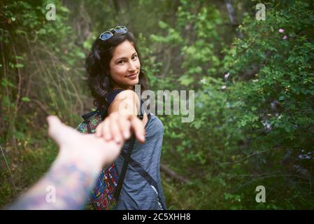 Porträt einer glücklichen jungen Frau, die die Hand ihres Freundes hält, während sie den Berg hinuntergeht. Pärchen genießen einen Spaziergang in der Natur. Stockfoto