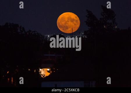 Wembley, Großbritannien. Juli 2020. UK Wetter - der Vollmond des Juli, bekannt als Buck Moon, steigt hinter Wembley im Nordwesten Londons auf. Im Bauernalmanach ist der Buck Moon so benannt nach dem neuen Geweih, das um diese Jahreszeit aus der Stirn eines Bocks hervortritt. Der Bogen des Stadions ist blau beleuchtet, um den 72. Geburtstag des National Health Service (NHS) zu feiern und allen NHS-Mitarbeitern für ihre Bemühungen während der laufenden Coronavirus-Pandemie zu danken. Kredit: Stephen Chung / Alamy Live Nachrichten Stockfoto