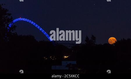 Wembley, Großbritannien. Juli 2020. UK Wetter - der Vollmond des Juli, bekannt als Buck Moon, erhebt sich hinter dem Wembley Stadium im Nordwesten Londons. Im Bauernalmanach ist der Buck Moon so benannt nach dem neuen Geweih, das um diese Jahreszeit aus der Stirn eines Bocks hervortritt. Der Bogen des Stadions ist blau beleuchtet, um den 72. Geburtstag des National Health Service (NHS) zu feiern und allen NHS-Mitarbeitern für ihre Bemühungen während der laufenden Coronavirus-Pandemie zu danken. Kredit: Stephen Chung / Alamy Live Nachrichten Stockfoto