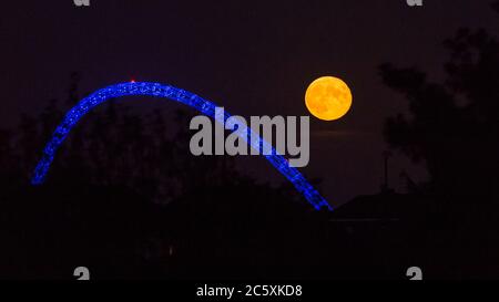 Wembley, Großbritannien. Juli 2020. UK Wetter - der Vollmond des Juli, bekannt als Buck Moon, erhebt sich hinter dem Wembley Stadium im Nordwesten Londons. Im Bauernalmanach ist der Buck Moon so benannt nach dem neuen Geweih, das um diese Jahreszeit aus der Stirn eines Bocks hervortritt. Der Bogen des Stadions ist blau beleuchtet, um den 72. Geburtstag des National Health Service (NHS) zu feiern und allen NHS-Mitarbeitern für ihre Bemühungen während der laufenden Coronavirus-Pandemie zu danken. Kredit: Stephen Chung / Alamy Live Nachrichten Stockfoto