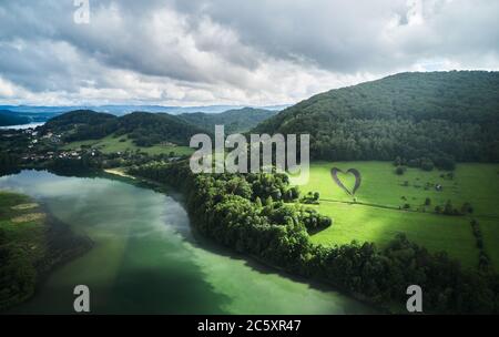 Herzform auf einem grünen Hügel, umgeben von Bergen, Bäumen, Fluss und einsamer, leerer Straße. Liebeszeichen in Erinnerung an einen verlorenen Angehörigen in Myczkowce, Polen. Stockfoto