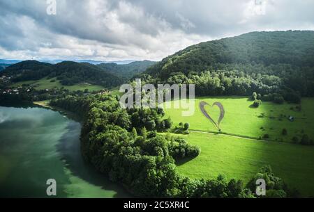 Herzform auf einem grünen Hügel, umgeben von Bergen, Bäumen, Fluss und einsamer, leerer Straße. Liebeszeichen in Erinnerung an einen verlorenen Angehörigen in Myczkowce, Polen. Stockfoto