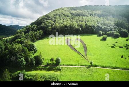 Herzform auf einem grünen Hügel, umgeben von Bergen, Bäumen, Fluss und einsamer, leerer Straße. Liebeszeichen in Erinnerung an einen verlorenen Angehörigen in Myczkowce, Polen. Stockfoto