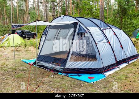 Camping im Freien - Zelte, Ausrüstung und Kochen. Blick auf den Campingplatz in der Natur. Ein großes Zelt steht auf einer grünen Wiese. Stockfoto