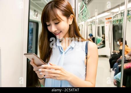Junge Frau, die das Handy in der U-Bahn beobachtet Stockfoto