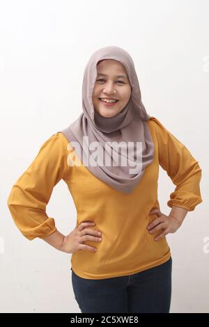 Erfolgreiche glücklich asiatische muslimische Frau trägt Hijab freundlich lächelnd mit Händen auf Hüften, zuversichtlich starke Geste, Seitenansicht Porträt isoliert auf weiß Stockfoto