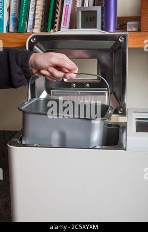 Frau, die eine Pfanne mit Zutaten in die Brotbackmaschine legt Stockfoto