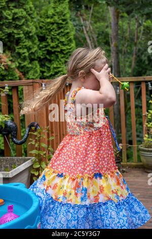 Drei Jahre alt Spaß haben spielen draußen Spaß Spinnen in Kreisen außerhalb mit einem ihrer Wasserspielzeug an ihrem Forhead gehalten Stockfoto