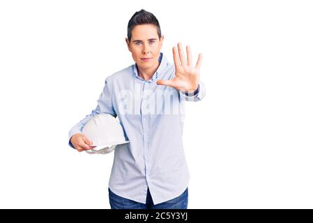 Junge Frau mit kurzen Haaren hält Architekt Hardhut mit offener Hand tun Stop-Zeichen mit ernsten und selbstbewussten Ausdruck, Verteidigung Geste Stockfoto