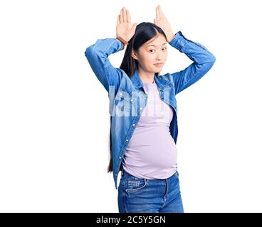 Junge schöne chinesische Frau schwanger erwarten Baby tun Bunny Ohren Geste mit Händen Handflächen zynisch und skeptisch. osterkaninchen Konzept. Stockfoto